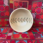 A small off-white ceramic bowl with a black and green geometric Palestinian embroidery pattern of a palm tree on the inside, displayed on a vibrant Palestinian textile background.
