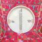 A round white ceramic plate with traditional geometric and floral patterns, displayed on a  colorful Palestinian embroidered textile. 